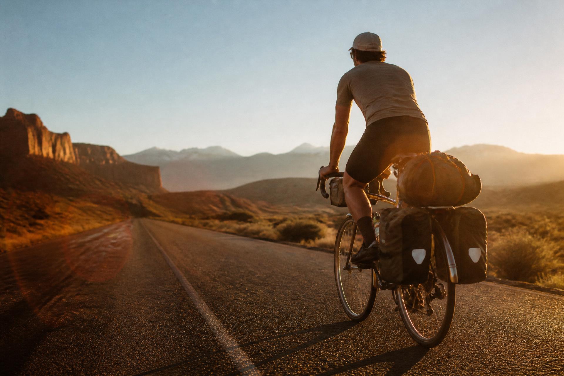 Cyclist riding a loaded touring bike on an open desert highway through the American West at golden hour